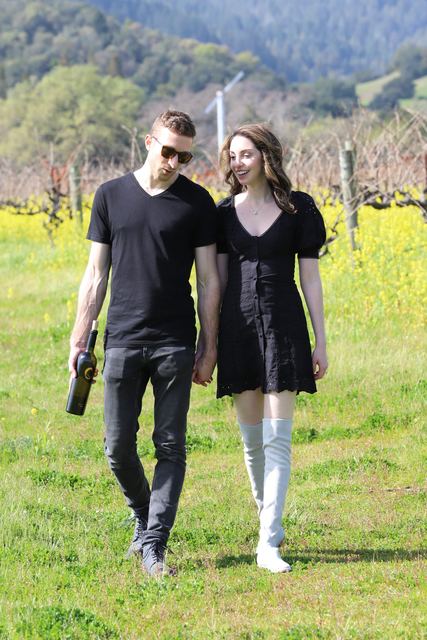 A newly engaged couple walking hand in hand through the vineyard