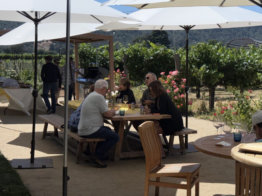Members having lunch at a table under white umbrellas beside the vineyard